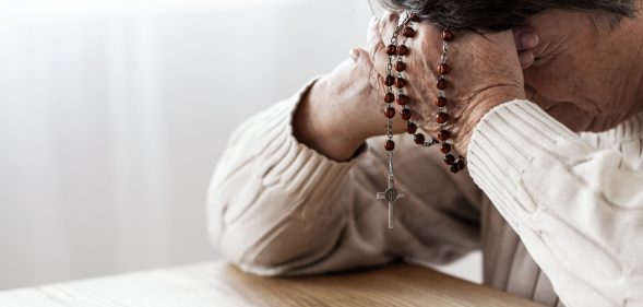 A man clutching rosary beads to his head