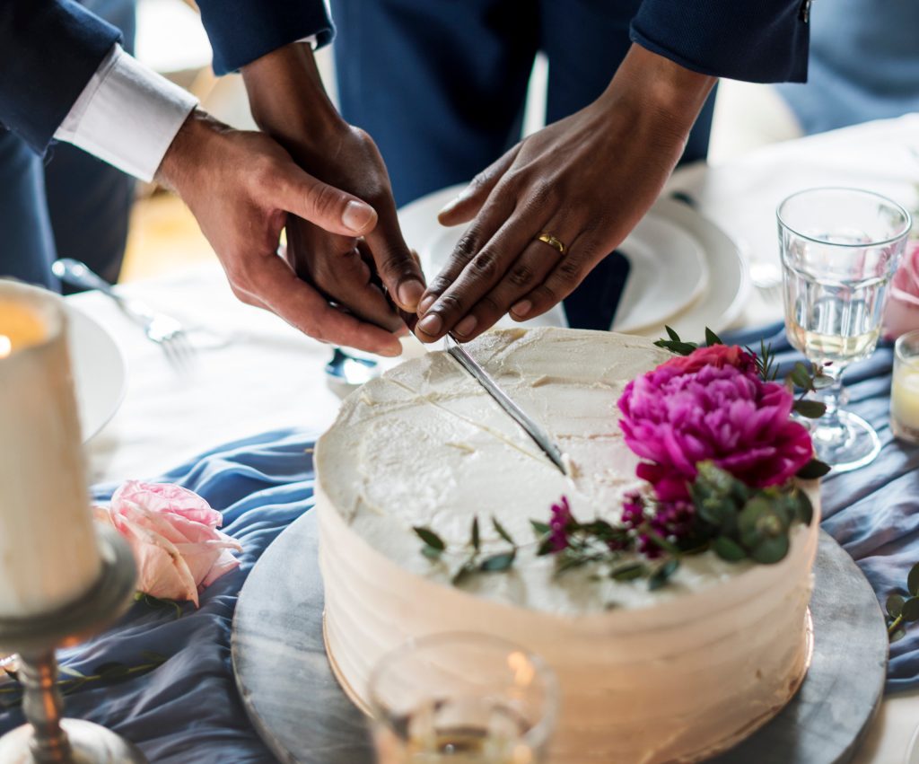 Close-up of two male hands cutting a wedding cake