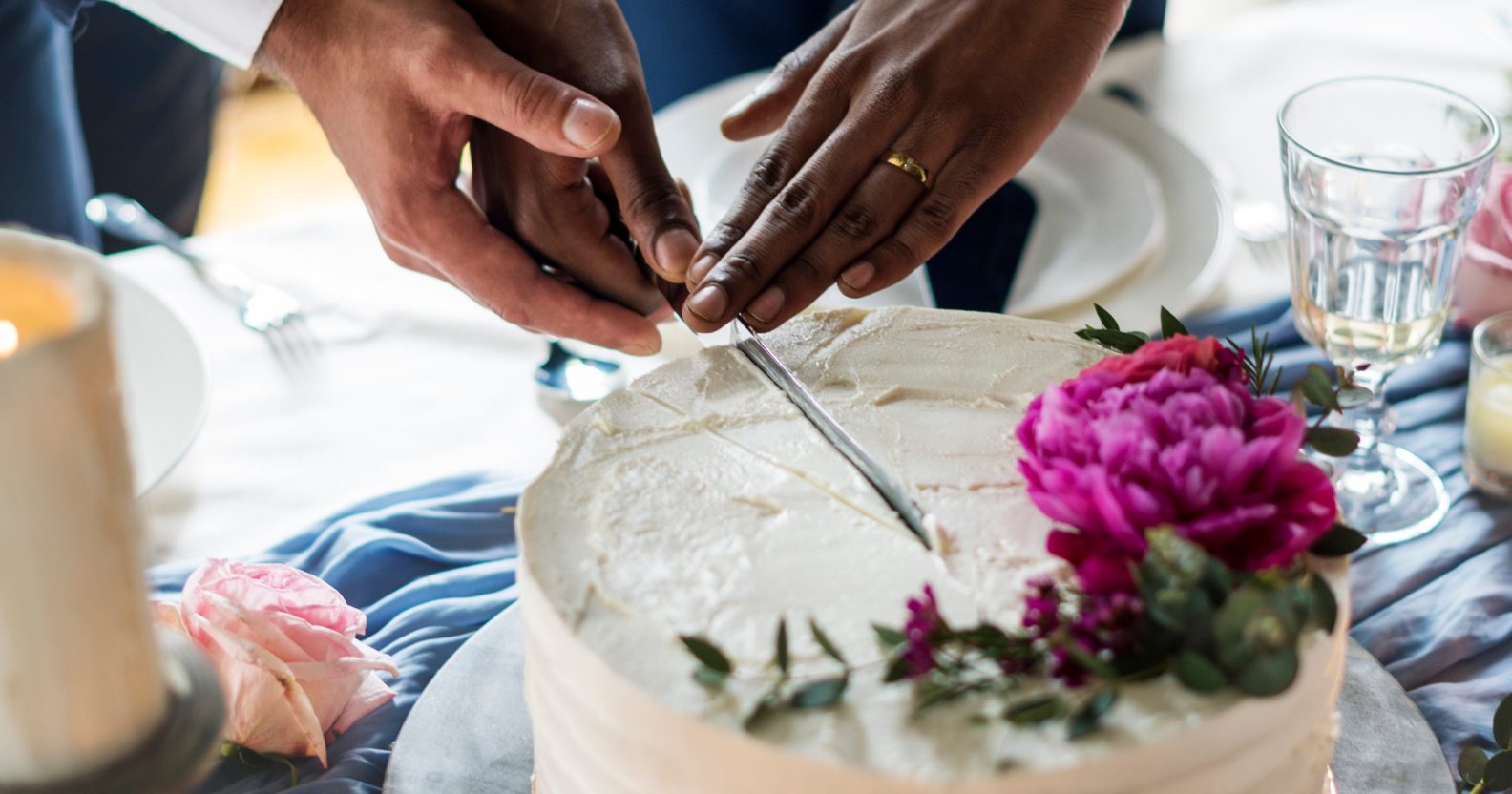 Close-up of two male hands cutting a wedding cake
