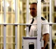 Stock photograph of a prison warden outside jail cell bars