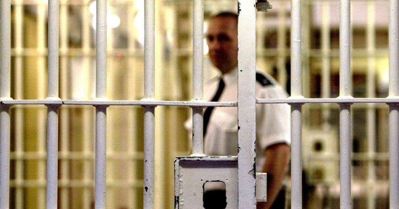 Stock photograph of a prison warden outside jail cell bars