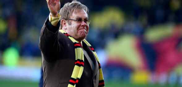 Elton John wearing a Watford FC scarf on a football pitch