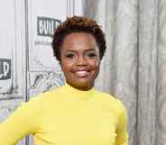 Karine Jean-Pierre wearing a yellow dress with long sleeves and a high neck, smiling
