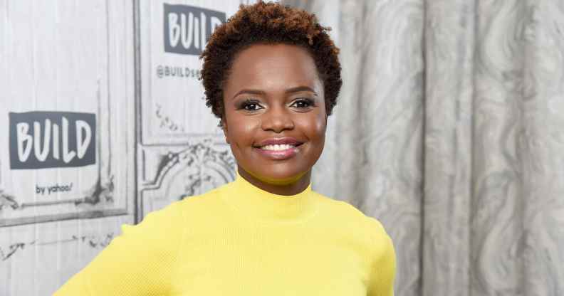 Karine Jean-Pierre wearing a yellow dress with long sleeves and a high neck, smiling