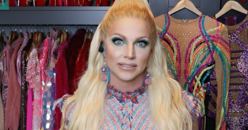 Courtney Act in a drag closet with a rail of glittering dresses behind her