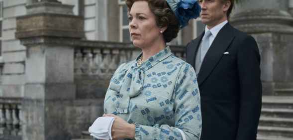 Olivia Colman as the Queen standing on the steps of the palace with Prince Philip behind her, in a duck-egg blue pussy-bow and pillbox hat