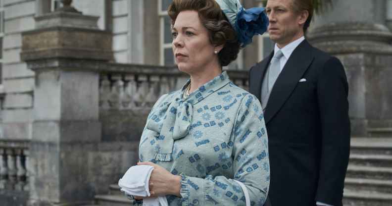 Olivia Colman as the Queen standing on the steps of the palace with Prince Philip behind her, in a duck-egg blue pussy-bow and pillbox hat