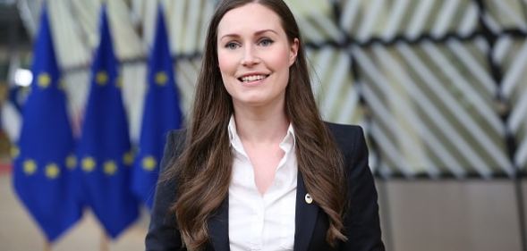 Sanna Marin is smiling in front of EU flags.