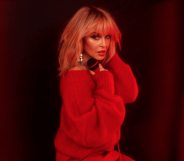 Kylie Minogue looking over her shoulder in a red jumper, a soft red neon lighting her face. She's holding a microphone