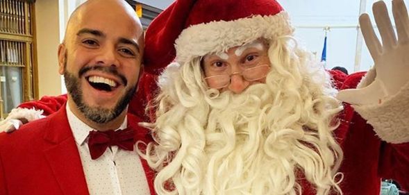 Queer Latino volunteer elf Michael Muñoz poses with Santa.