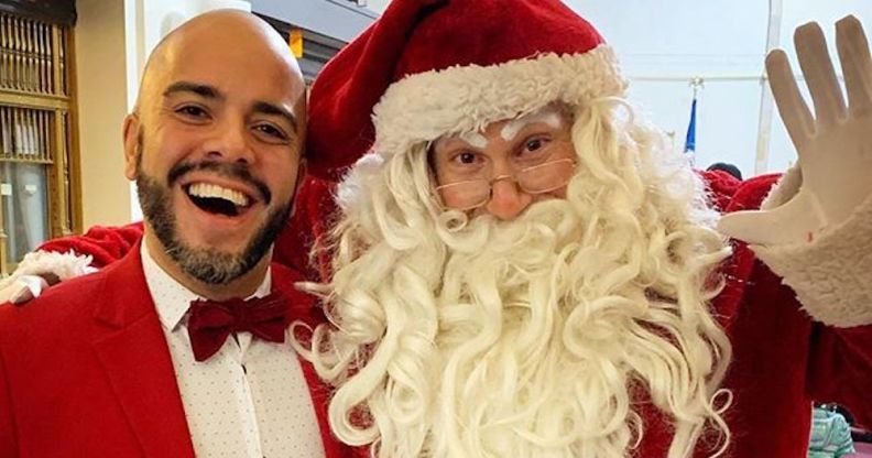 Queer Latino volunteer elf Michael Muñoz poses with Santa.