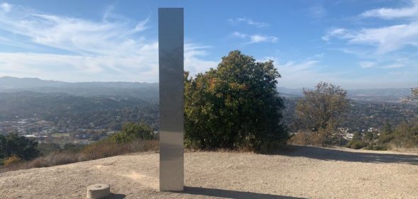 A tall, slim silver monolith at the top of an empty hill