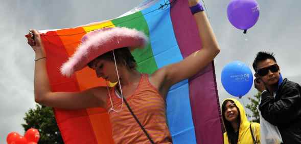 A Pride-goer in a pink cowboy hat with a rainbow flag around her back