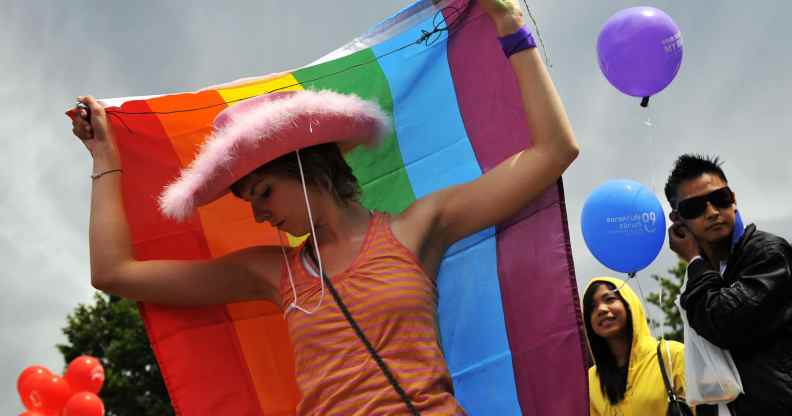 A Pride-goer in a pink cowboy hat with a rainbow flag around her back