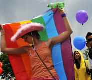 A Pride-goer in a pink cowboy hat with a rainbow flag around her back