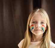 A child with rainbow LGBT+ Pride flag face paint on each of her cheeks