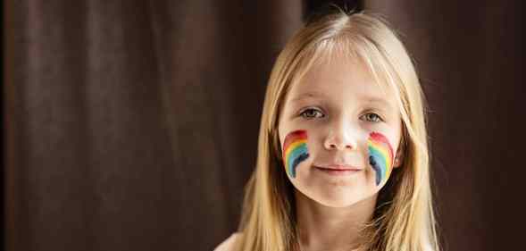A child with rainbow LGBT+ Pride flag face paint on each of her cheeks