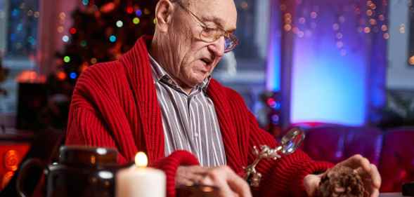 Portrait of a concentrated and serious santa claus working at table and preparing decoration from cone in colourful and decorated cosy room.