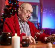 Portrait of a concentrated and serious santa claus working at table and preparing decoration from cone in colourful and decorated cosy room.