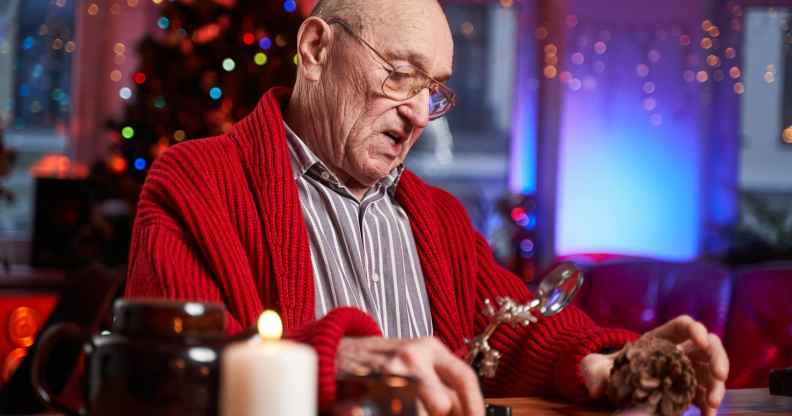 Portrait of a concentrated and serious santa claus working at table and preparing decoration from cone in colourful and decorated cosy room.