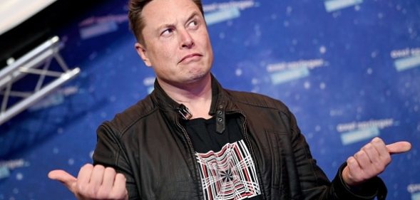 Elon Musk gestures while wearing a graphic print t-shirt and a black jacket