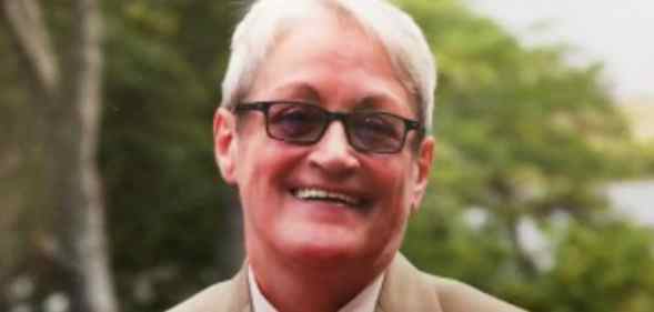 Carmen Vázquez smiles in a beige suit, white shirt and orange tie