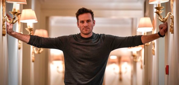 Armie Hammer stretches his arms outwards towards the corridor walls
