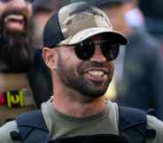 Proud Boy leader Enrique Tarrio smile while wearing a dark green t-shirt and cap