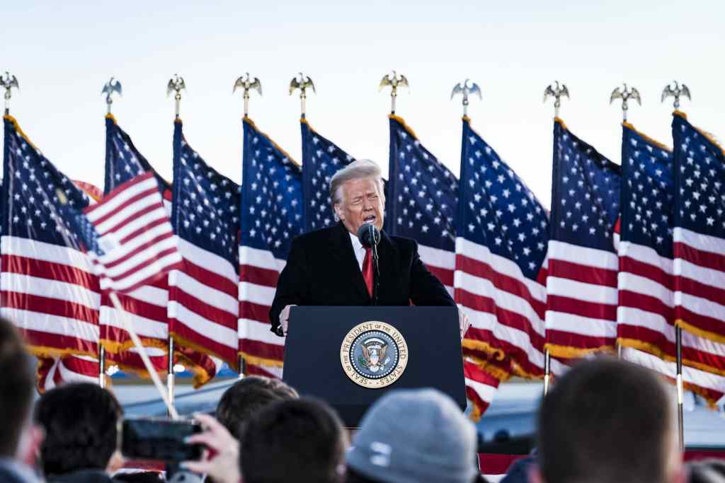 President Donald Trump speaks to his supporters on stage, American flags behind him