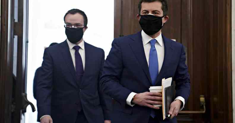 Pete Buttigieg and Chasten Buttigieg, both wearing suits, walk through the doors in the Senate