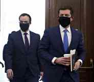 Pete Buttigieg and Chasten Buttigieg, both wearing suits, walk through the doors in the Senate