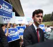 Jon Ossoff in a suit speaks to reporters while supporters hold up signs