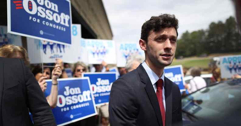 Jon Ossoff in a suit speaks to reporters while supporters hold up signs