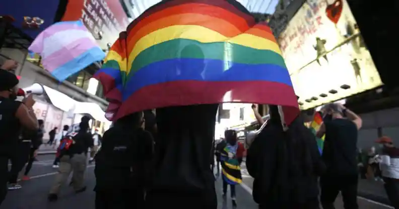 Americans holding a pride flag and trans flag in the background during a protest.