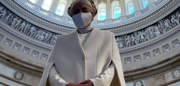 Lady Gaga in a white sheath cape and face mask, the rotunda of the Capitol complex framing her like a halo,