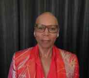 RuPaul out of drag, wearing glasses and a red shirt and blazer