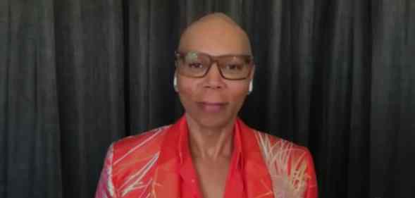 RuPaul out of drag, wearing glasses and a red shirt and blazer