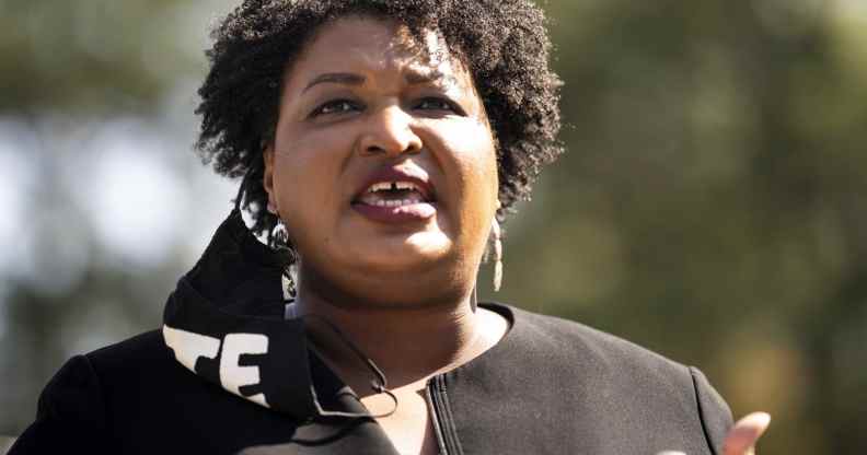Close-up of Stacey Abrams speaking. A black face mask with 'VOTE' in bold white text is hanging from one ear.