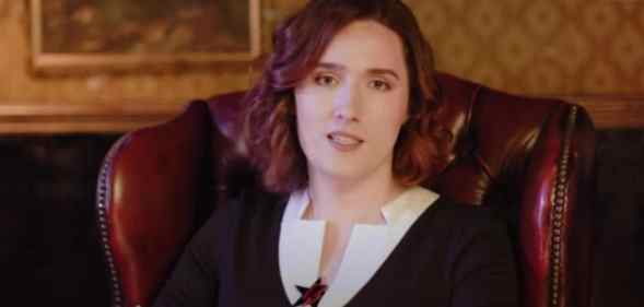 Abigail Thorn sitting on a leather chair wearing a white shiny and black v-neck jumper