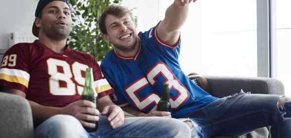 Two men in football tops holding beer bottles