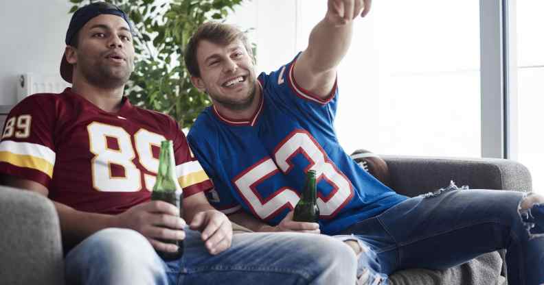 Two men in football tops holding beer bottles