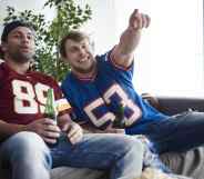 Two men in football tops holding beer bottles