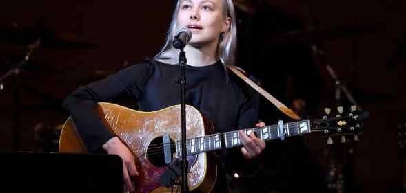 Phoebe Bridgers performs on stage holding a guitar