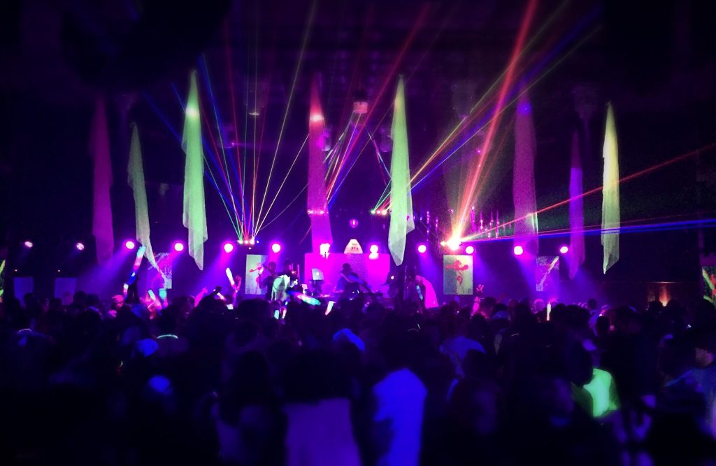 A photograph of a night-club, purple and green flights flashing a crowd a clubbers