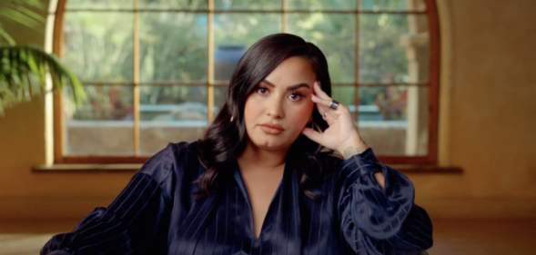 Demi Lovato in the trailer for her documentary, sitting on a chair resting her hand on her face
