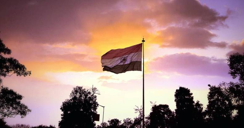 A photo of the national flag of India showing trees in the background and a pink/orange sunset sky