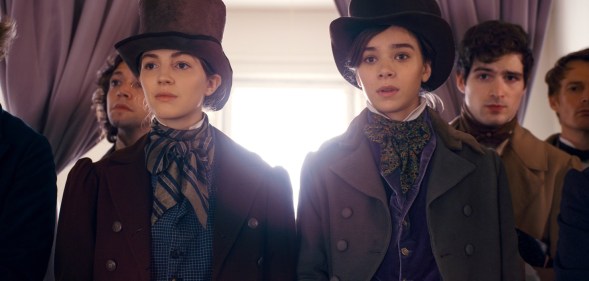 Ella Hunt and Hailee Steinfeld wearing top hats and period garbs in front of a window