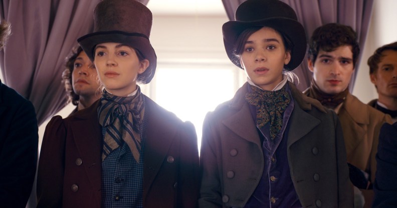 Ella Hunt and Hailee Steinfeld wearing top hats and period garbs in front of a window