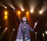 Manizha Sangin holds her microphone in the air against a constellation of spotlights