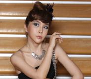 Harisu poses in a black dress and necklace against stairs